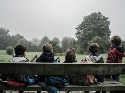 five children sitting on bench front of trees